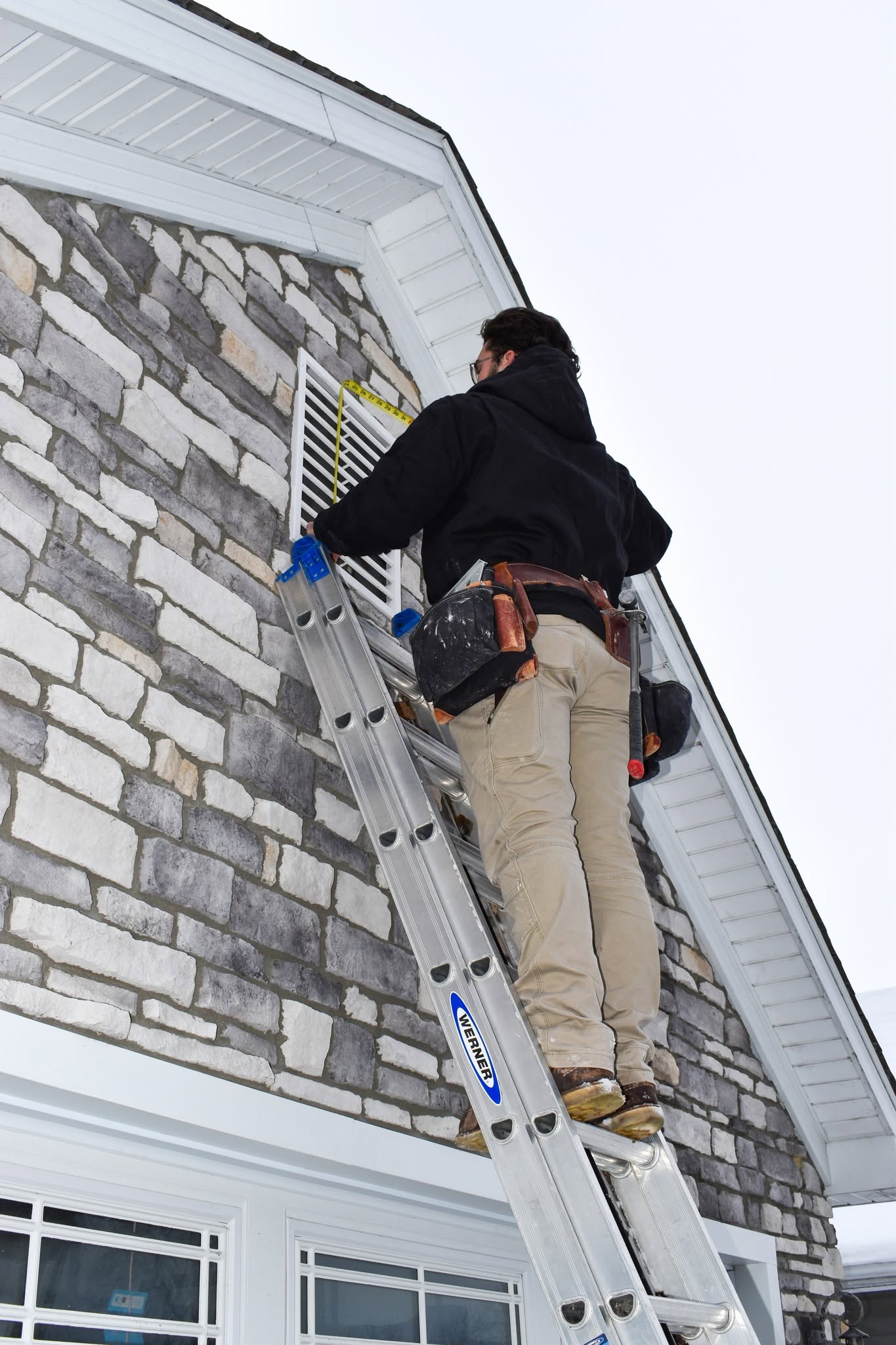 Snoble Construction crew member working on exterior stonework from a ladder