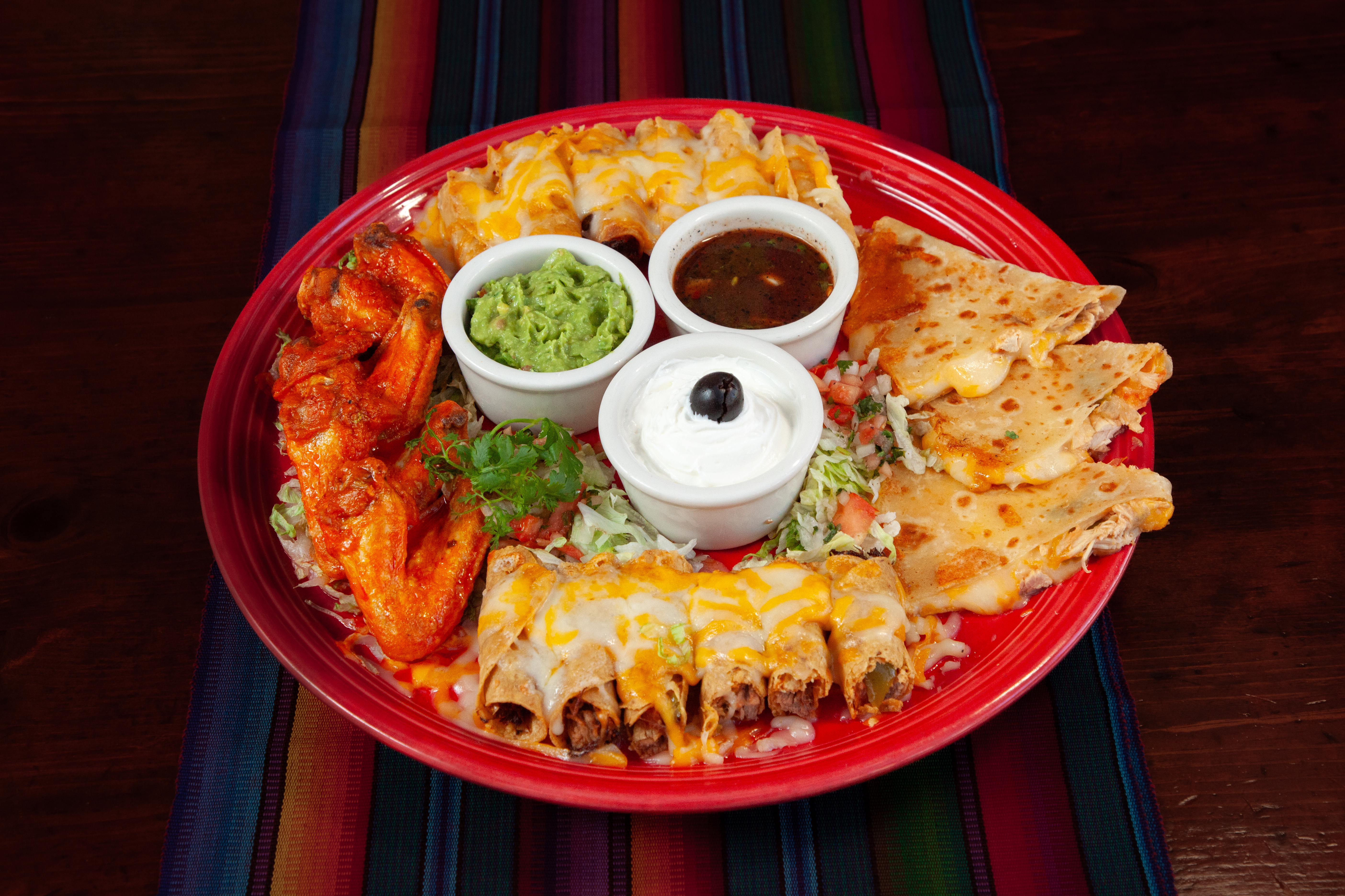Casa de Pico botanas platter with taquitos, quesadilla wedges and red chicken wings around cups of fresh guacamole, sour cream and salsa