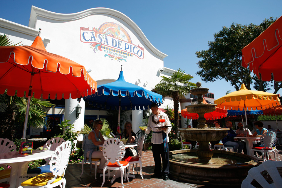 Exterior of Casa de Pico with colorful signage, potted plants, and guests entering the restaurant at dusk