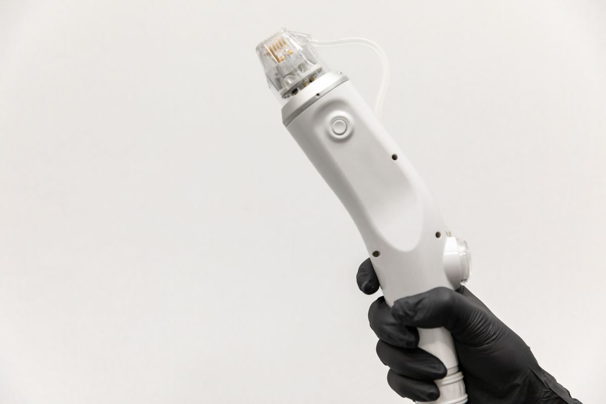 Mano con guante sosteniendo un dispositivo de microneedling sobre fondo blanco