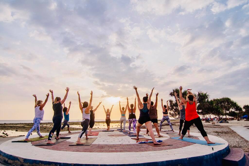 Yoga group on the beach at sunrise, arms raised