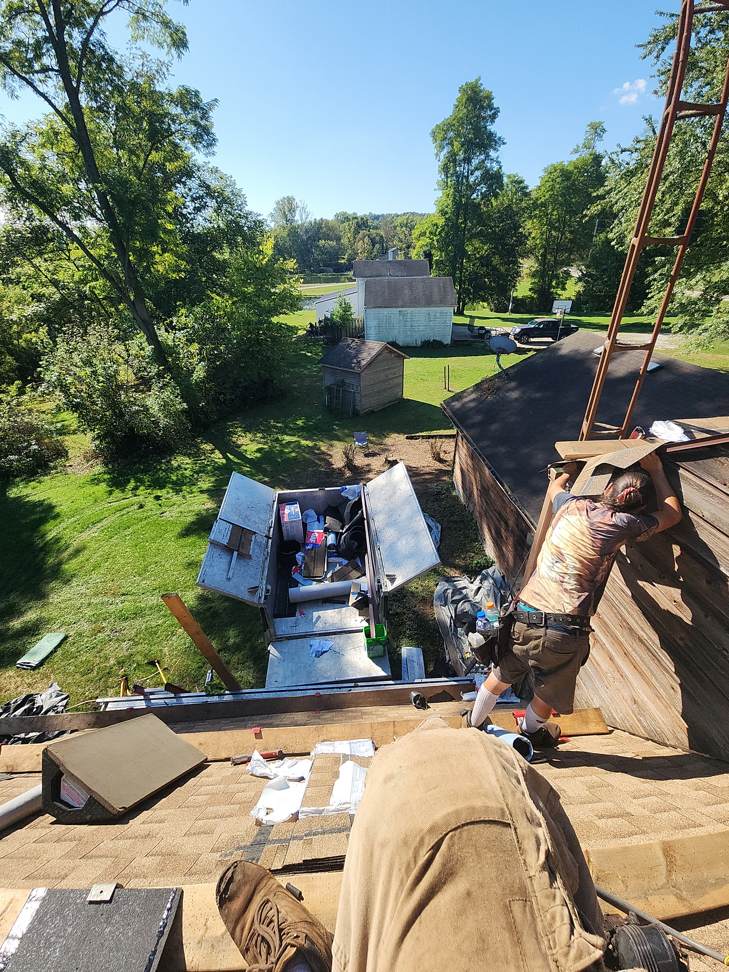Weikles Roofing crew members actively working on a steep residential roof replacement project, with materials and equipment staged below on a beautiful sunny day. - Weikles Roofing Weikles Roofing crew members actively working on a steep residential roof replacement project, with materials and equipment staged below on a beautiful sunny day. - Weikles Roofing