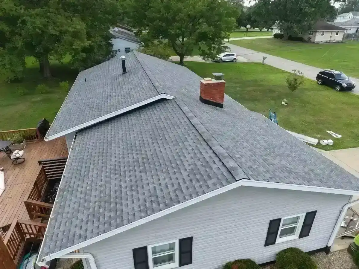 Aerial drone view of a large residential home featuring a recently installed dark charcoal asphalt shingle roof with multiple hip and gable sections, dormers, and clean ridge lines, set on a well-manicured property. - Weikles Roofing