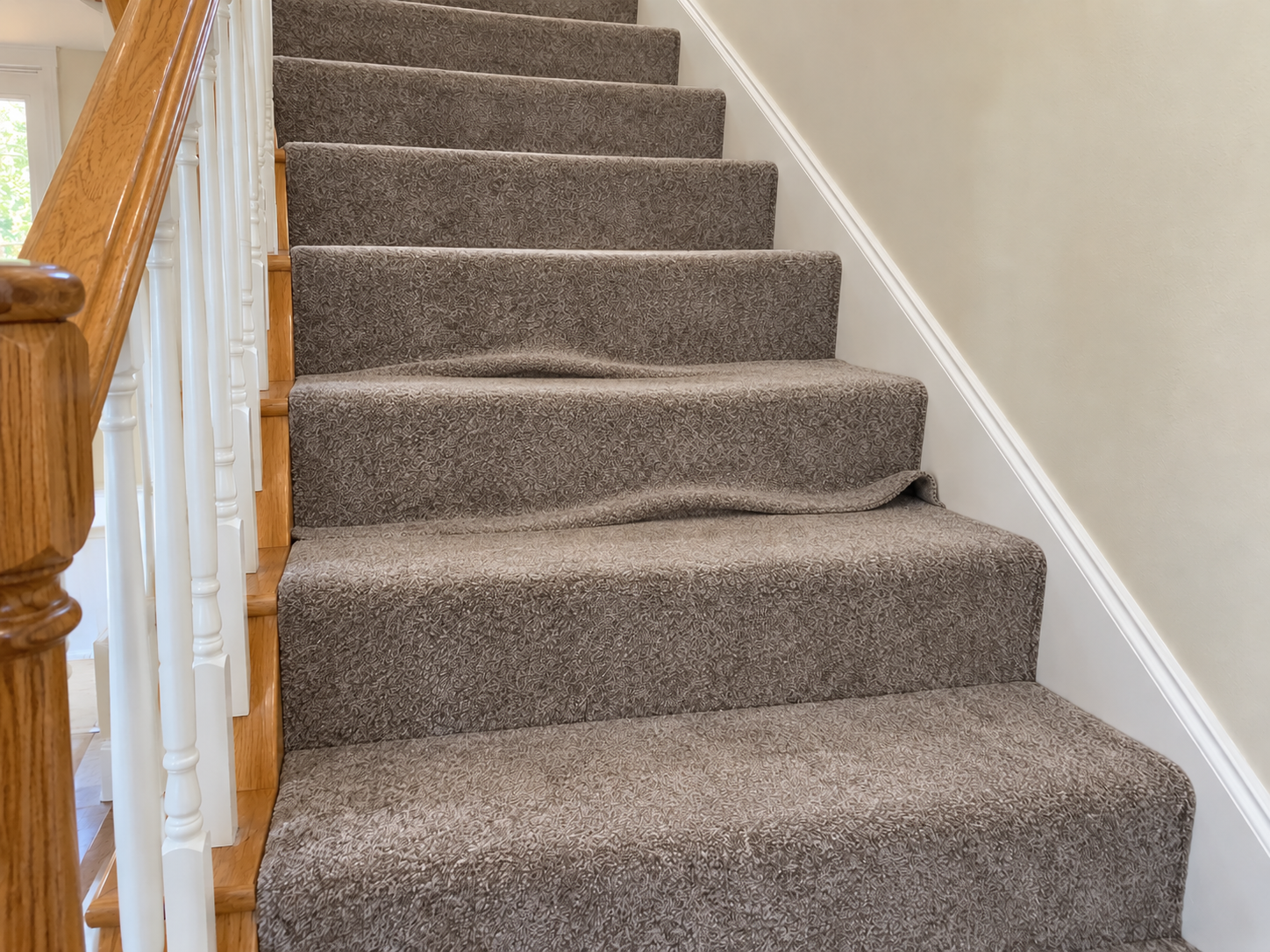 Before: loose taupe staircase carpet with a buckled, wrinkled fold sagging over one stair nose