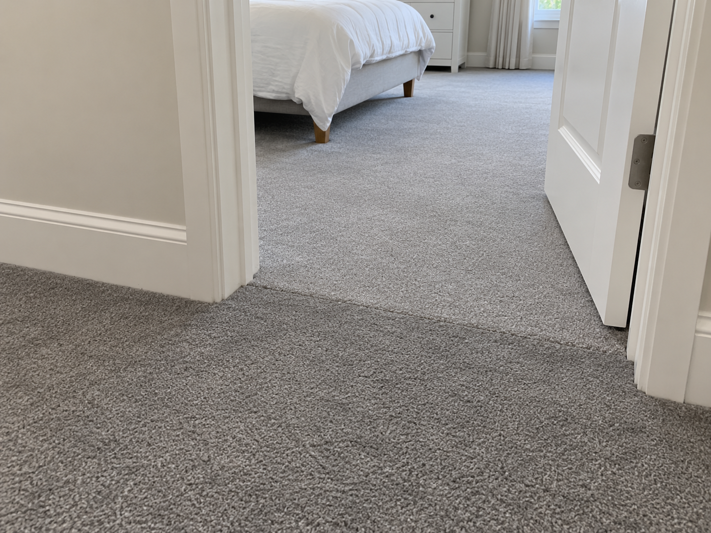 Before: bedroom doorway where lighter gray bedroom carpet meets darker gray hallway carpet with a sharp shade line at the seam