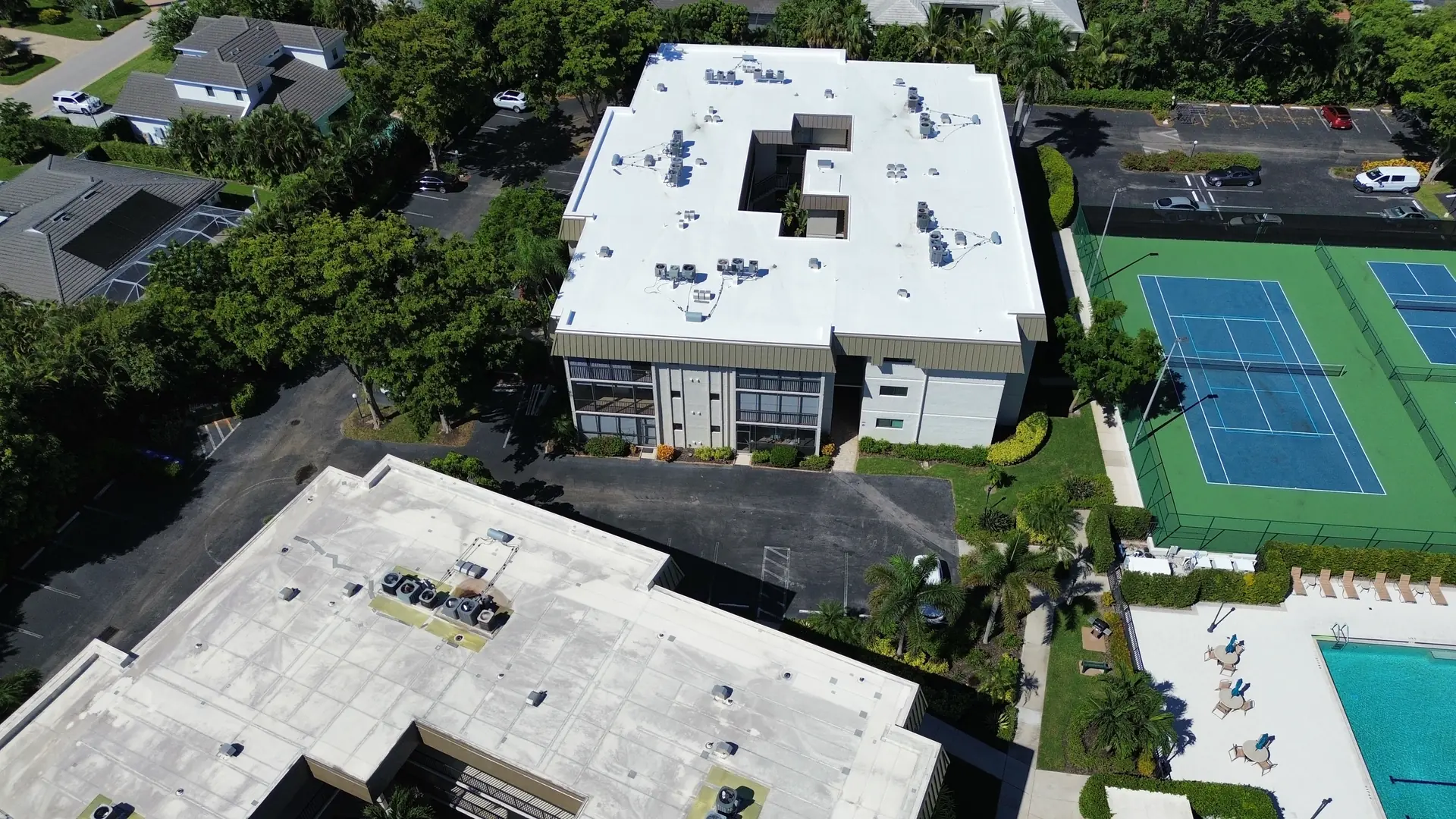 Condominium building with a white TPO roof beside the community tennis courts