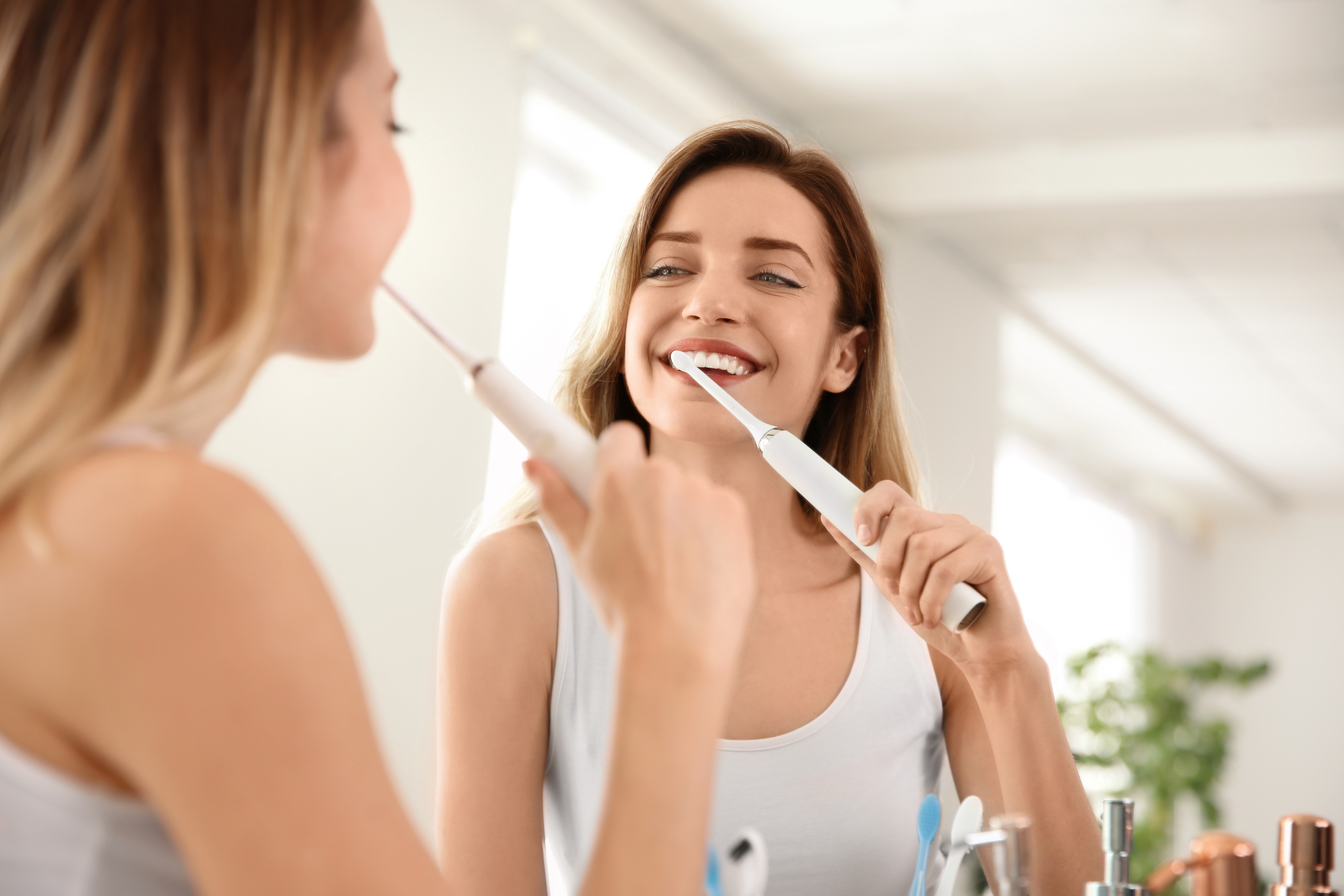 Middle aged caucasian woman with brown hair using an electric toothbrush looking in the mirror. 