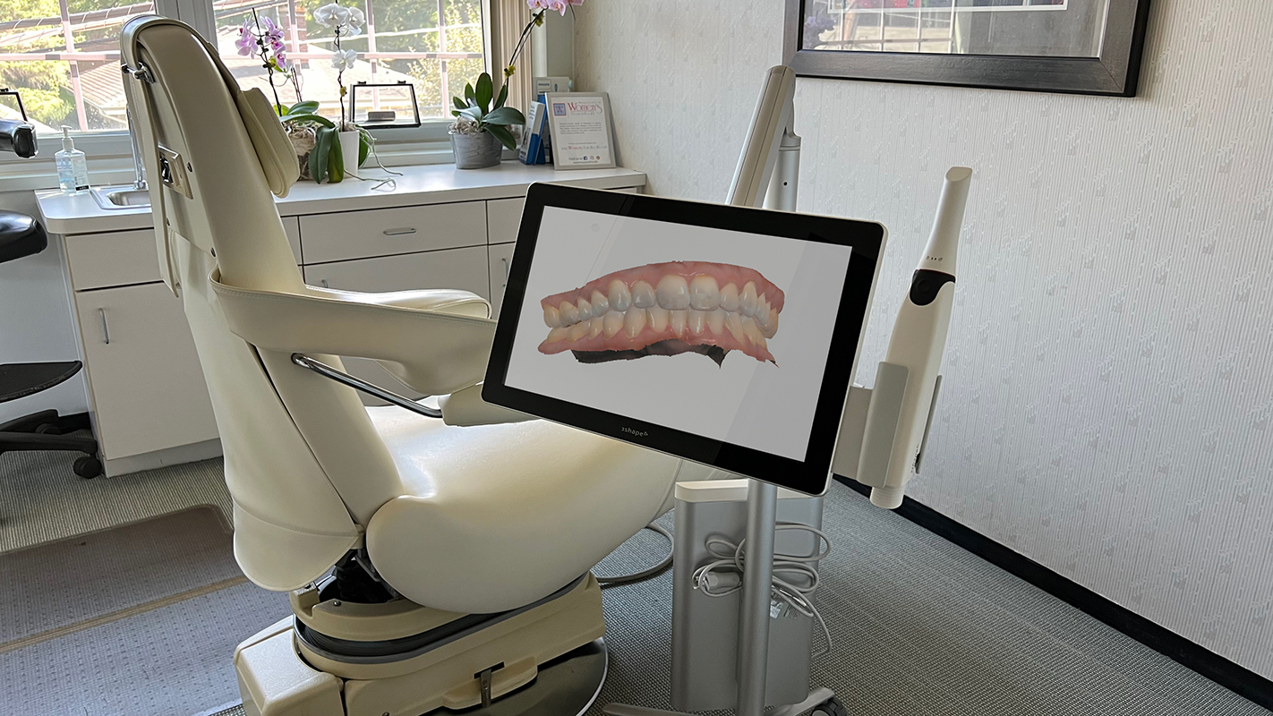 foreground a trios move+  scanner with screen displaying a 3d model of teeth. In the background a dental chair 