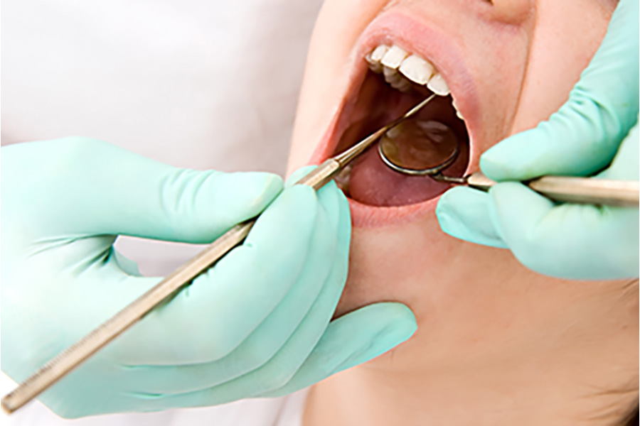 Photo of a closeup of a woman's mouth with dental probe and mirror being help by tw the mouth  hands wearing light green gloves