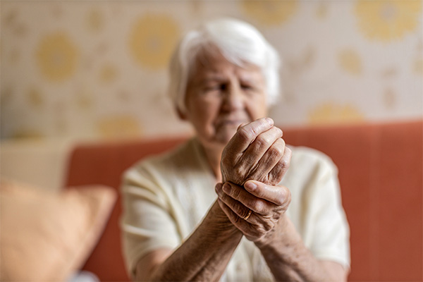 Senior woman with short white hair with hand on wrist, representing pain in her hand or wrist signifying osteoporosis' impact on gum disease risk.