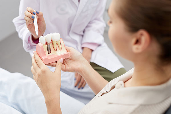 Dentist showing a female patient with brown hair  in a dental chair a model of teeth with an implant, representing periodontal implant process.