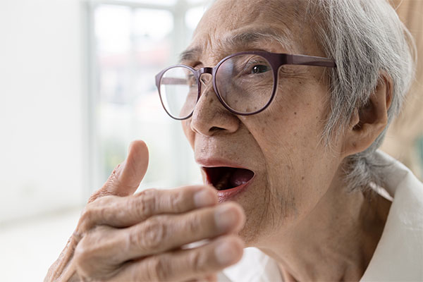 Elderly person covering mouth with hand, implying bad breath or taste due to oral health problems.