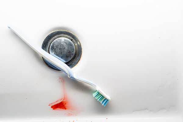 Toothbrush with blood in the bottom of the sink, near the drain stopper. 
