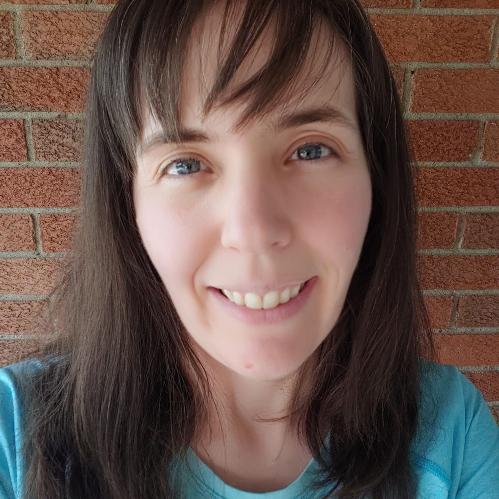 girl face - brown hair with bangs in teal shirt against brick wall