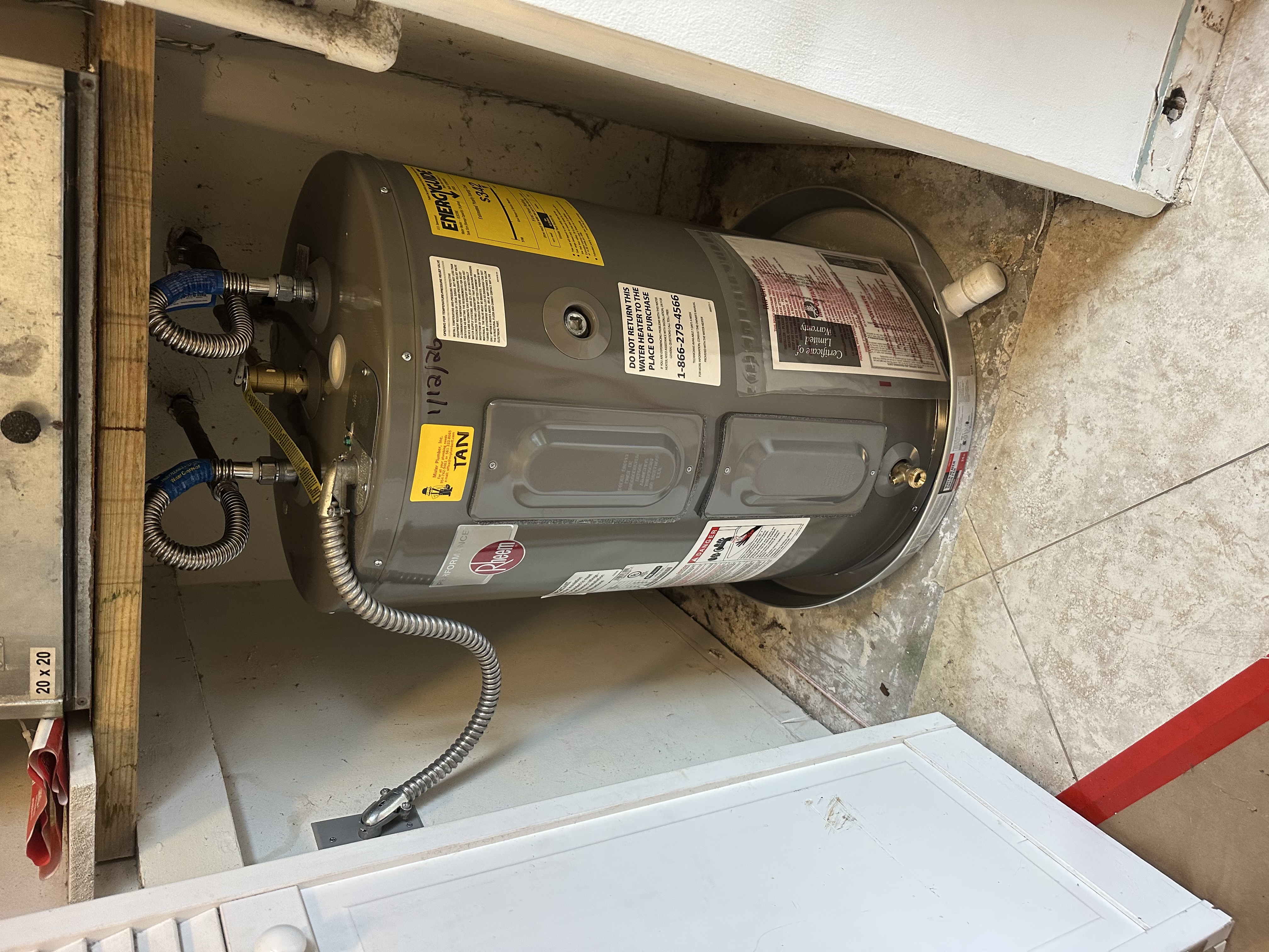 New Rheem electric water heater installed in a hall closet under the air handler, sitting in a drain pan with new flex lines