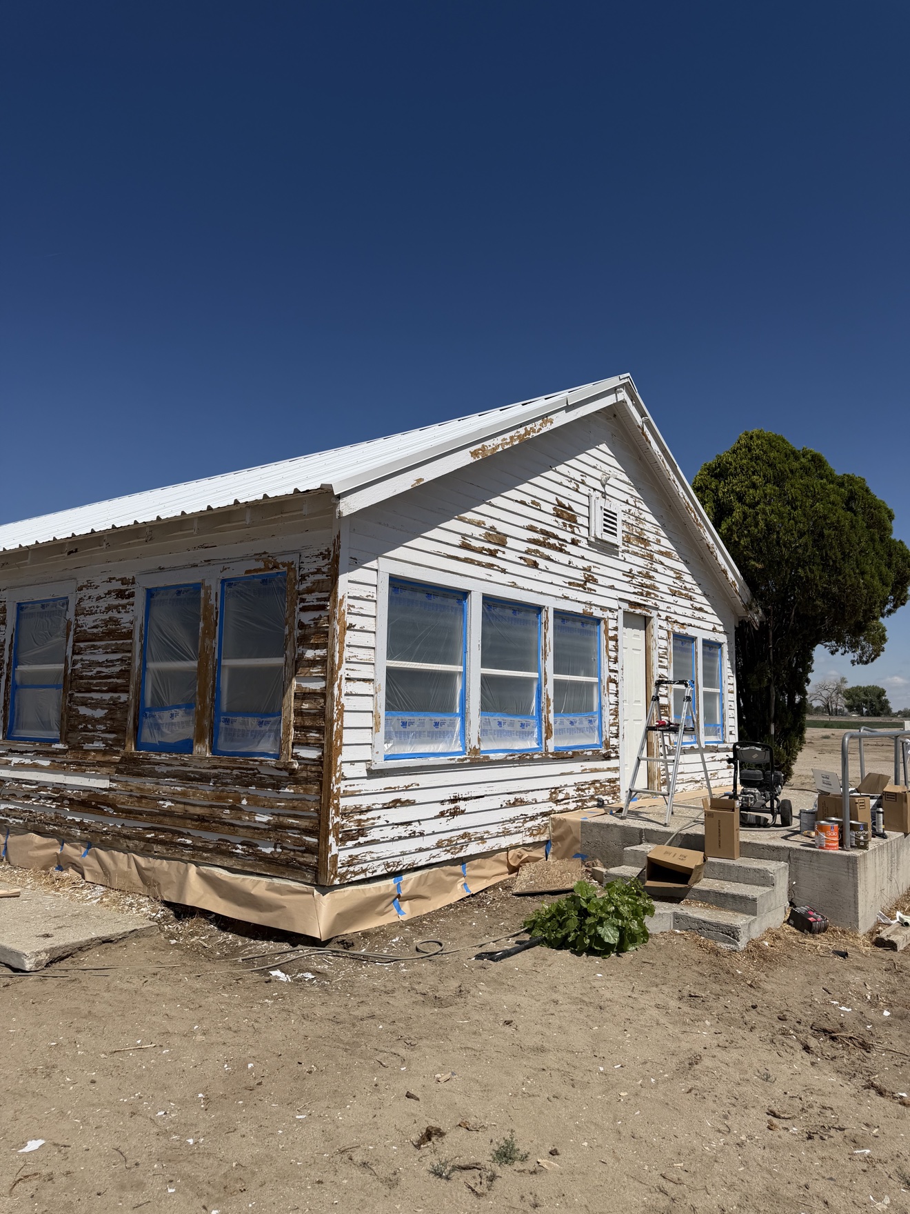 Exterior before repaint — front angle, peeling paint and masked windows