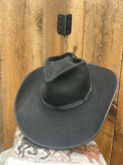 Black felt hat displayed against a wood plank wall, front angle