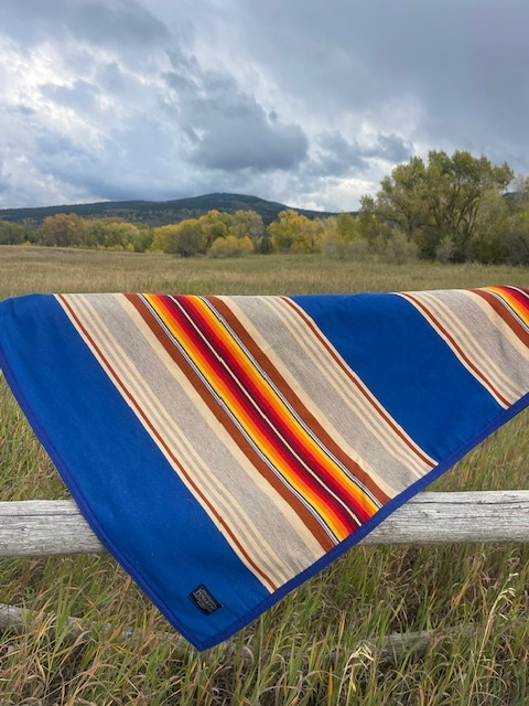 Striped wool blanket draped over a fence rail with fields and hills behind