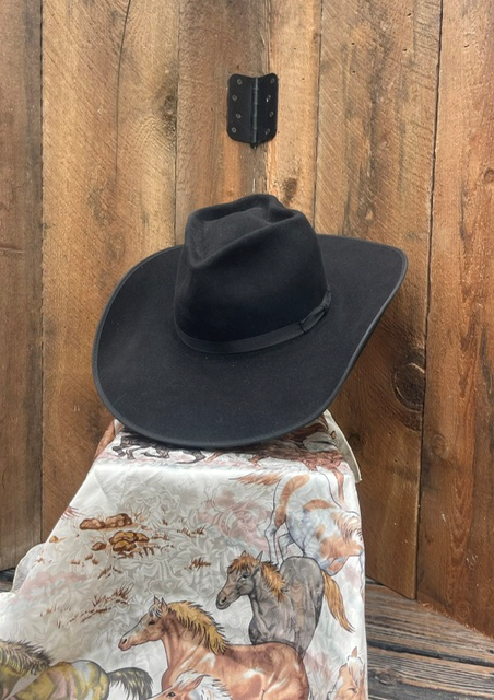 Black felt hat displayed on a horse-print scarf against a wood plank wall