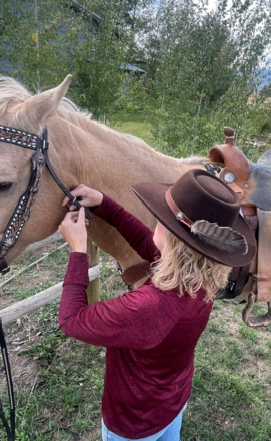 Woman in a feathered felt hat adjusting a horse's bridle