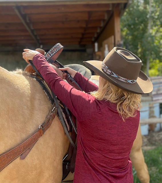 Woman in a beaded-band felt hat saddling a horse