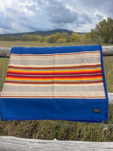 Striped wool blanket draped over a wooden fence in an open field