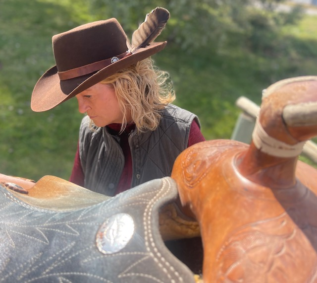 Woman in a feathered brown felt hat beside a saddle