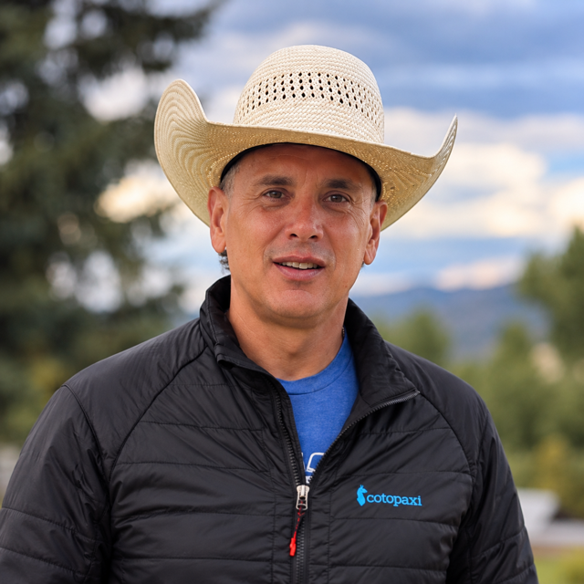 Man wearing a straw hat outdoors with mountains behind him