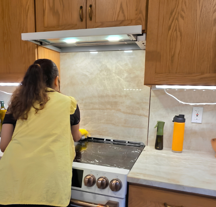 Cleaner in a yellow apron wiping a bright marble kitchen countertop