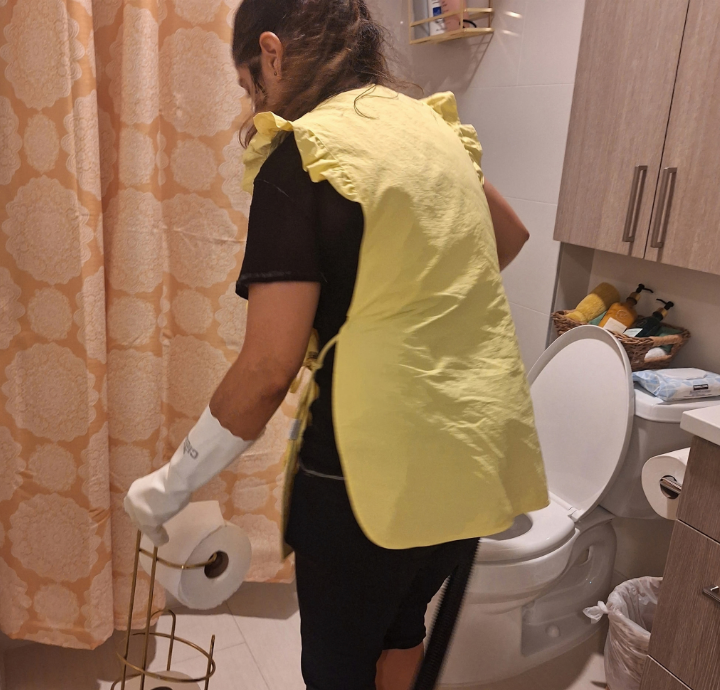Helena Shine cleaning professional in a yellow vest cleaning a bathroom in detail