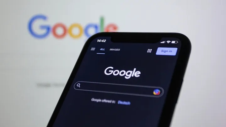 Phone showing the Google search page, with the Google logo on a screen behind it