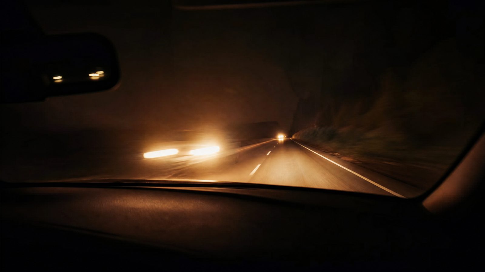 Des phares sur une route de campagne, vus depuis l'intérieur d'une voiture, la nuit