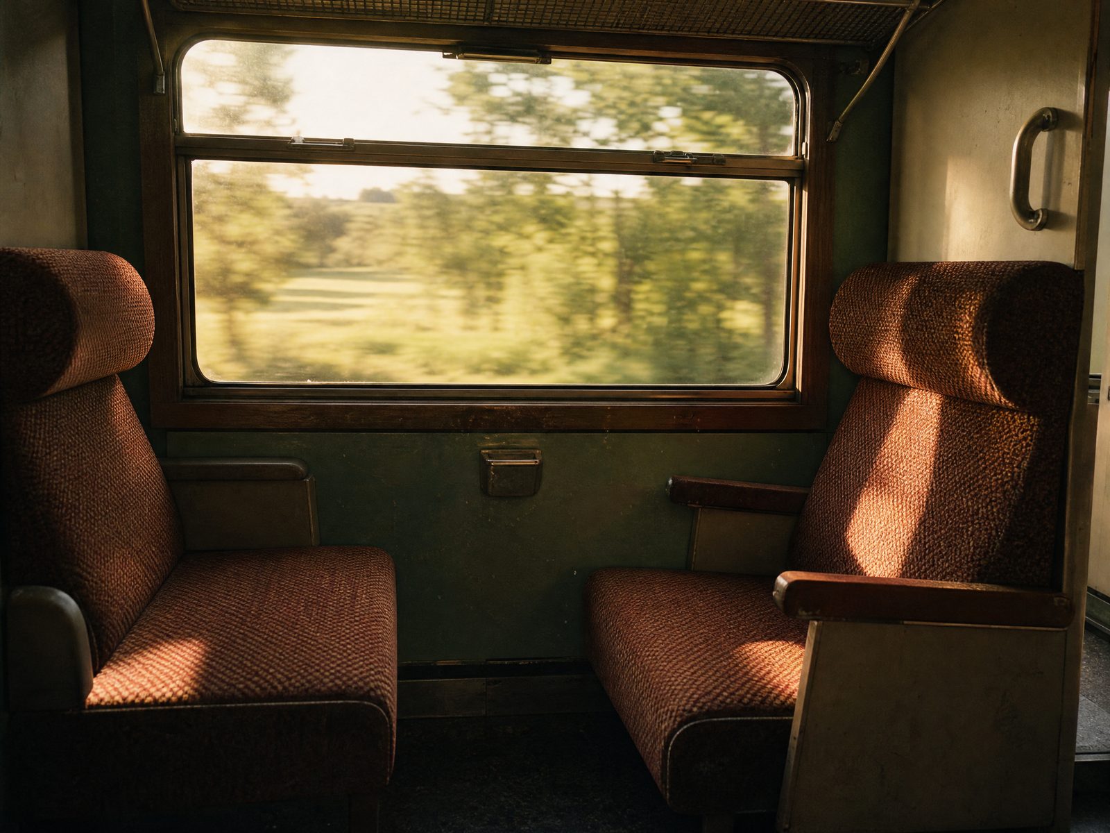 Deux banquettes de train en vis-à-vis, la campagne défilant derrière la vitre dans la lumière de fin d'après-midi