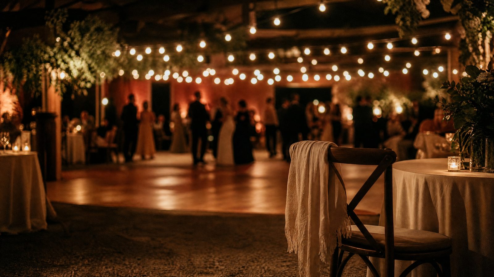 Une piste de danse de mariage vue de loin, guirlandes lumineuses, une chaise vide au premier plan