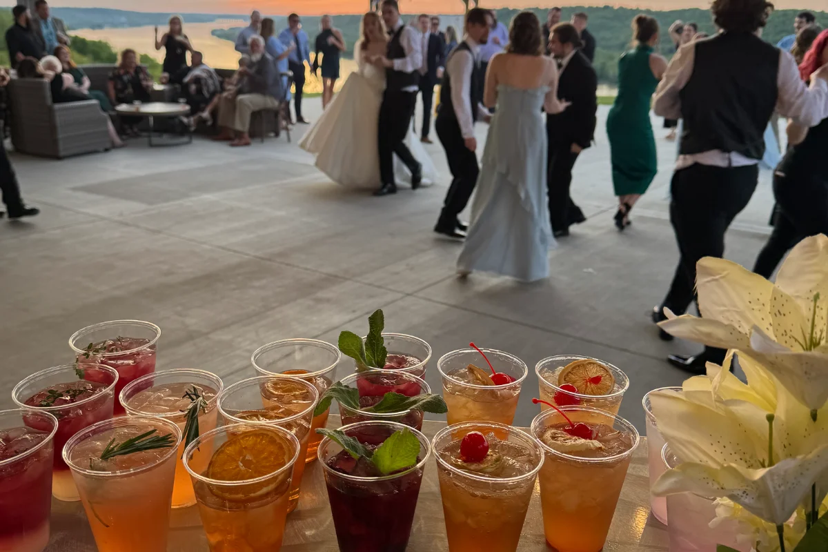 Bars on Wheels cocktails lined up at outdoor wedding reception with guests dancing near mobile bar