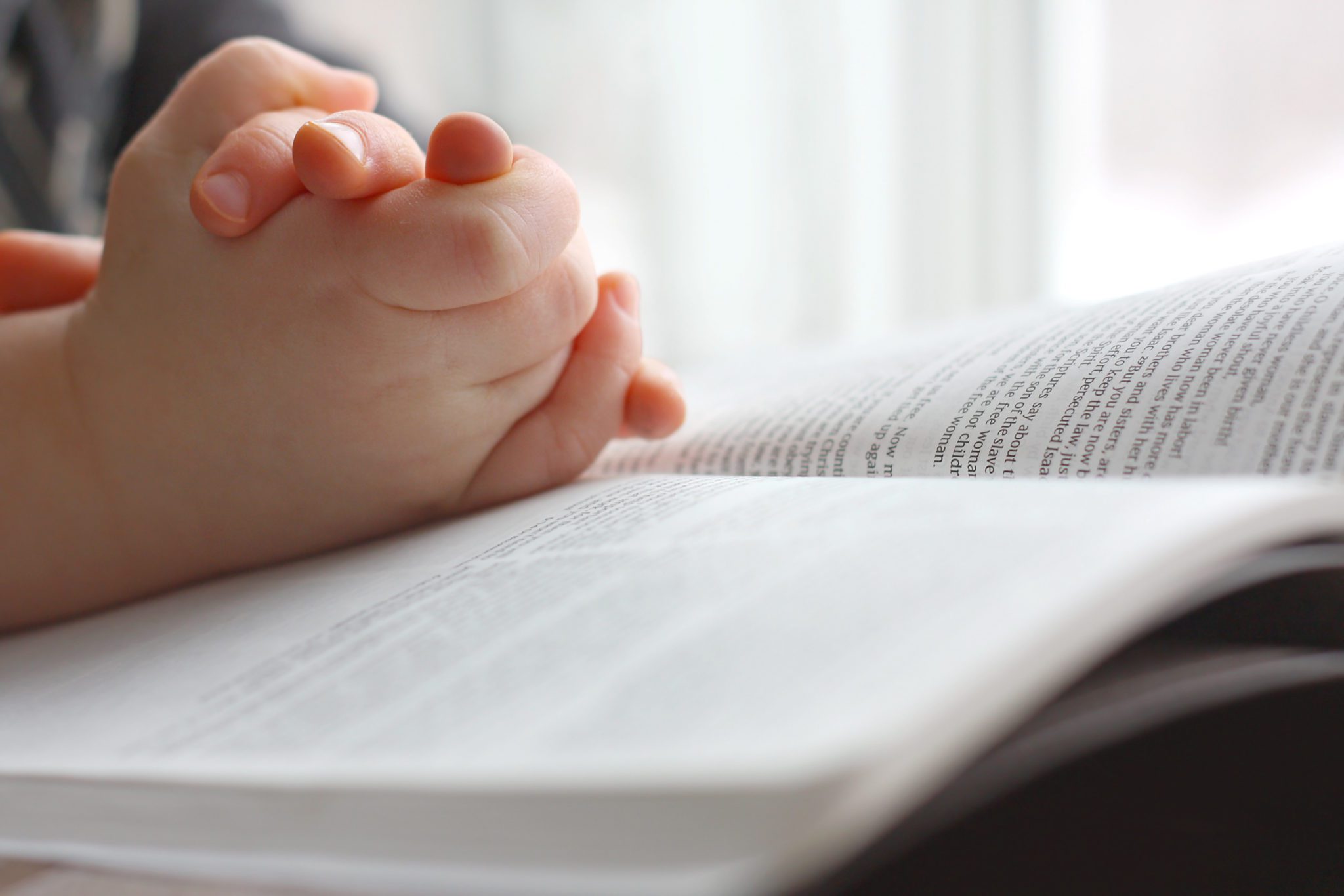 Child's hands praying on Bible