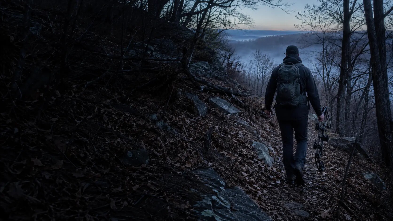 Bowhunter walking uphill through the woods before sunrise