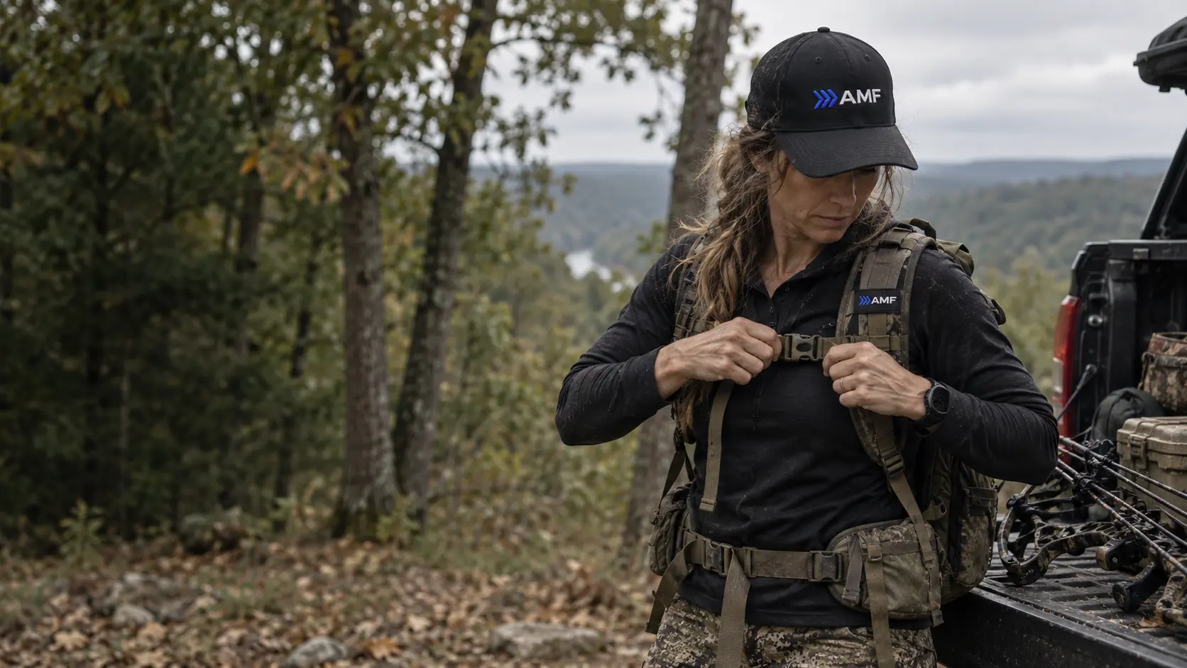 Woman in an AMF cap shouldering a pack on a wooded trail