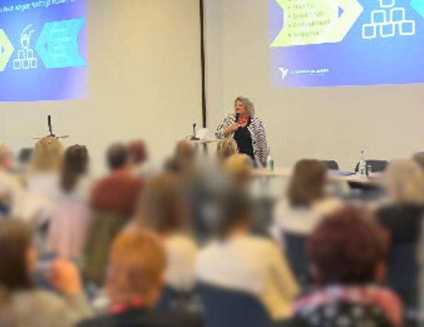 Large audience watching Birgit Gosejacob present — room-scale proof of speaking experience