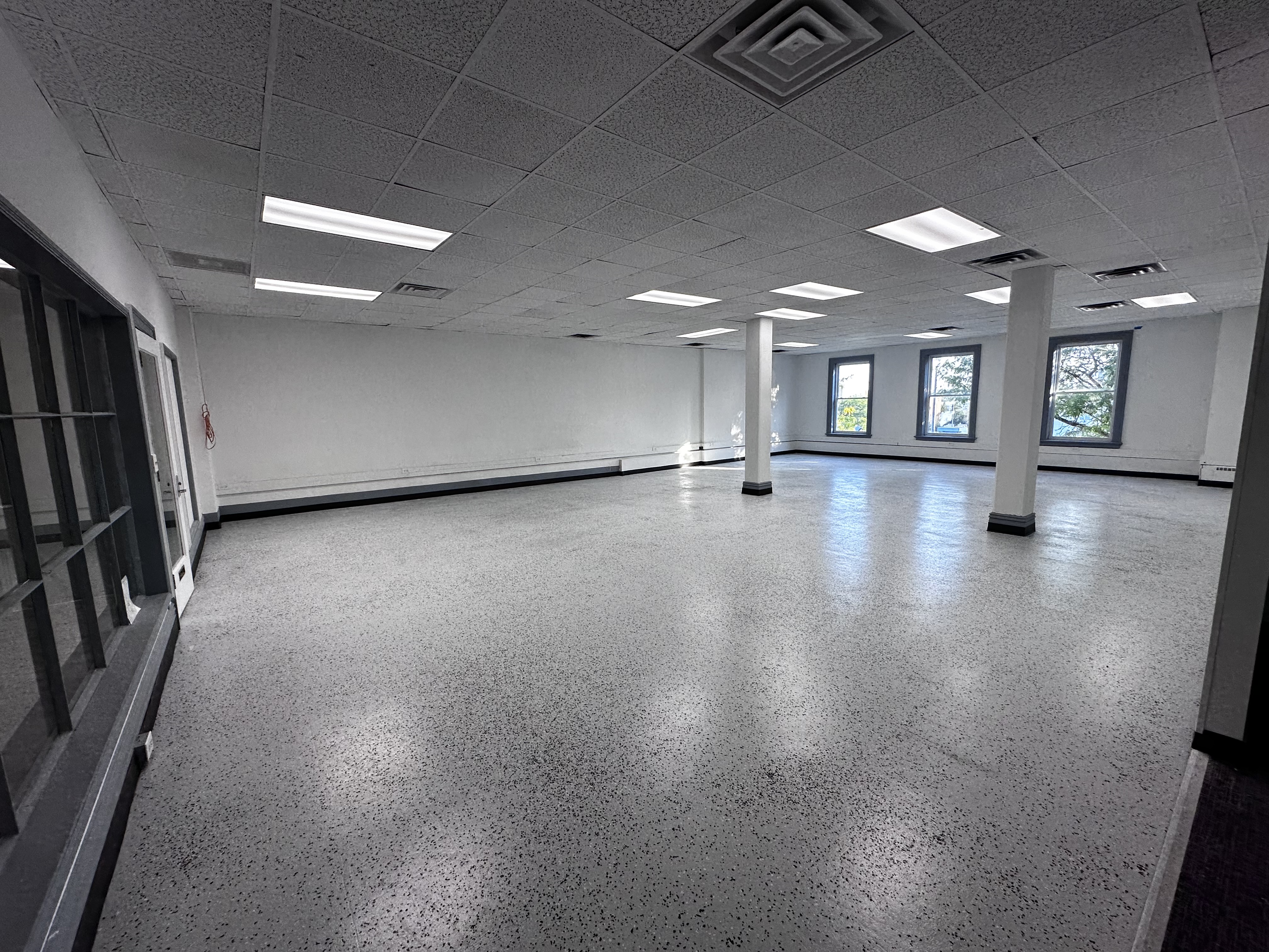 professional photorealistic wide-angle view of a bright neutral-toned 1500 square foot open-concept office suite in downtown Toledo, large windows with city street views, polished floors, minimal modern furnishings, subtle branding overlay text on glass wall