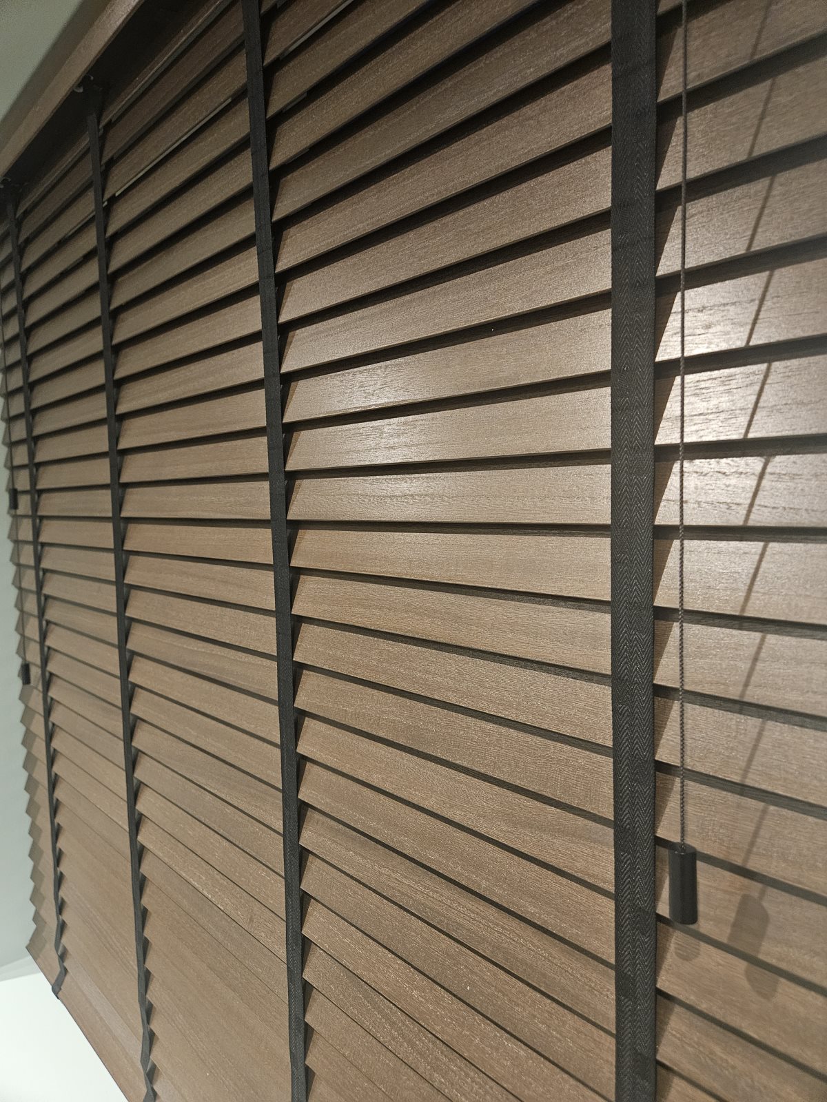 Close-up of closed walnut Venetian blind slats with black tapes and pull, fitted by Eclipse SBC near Bawtry Close-up of closed walnut Venetian blind slats with black tapes and pull, fitted by Eclipse SBC near Bawtry