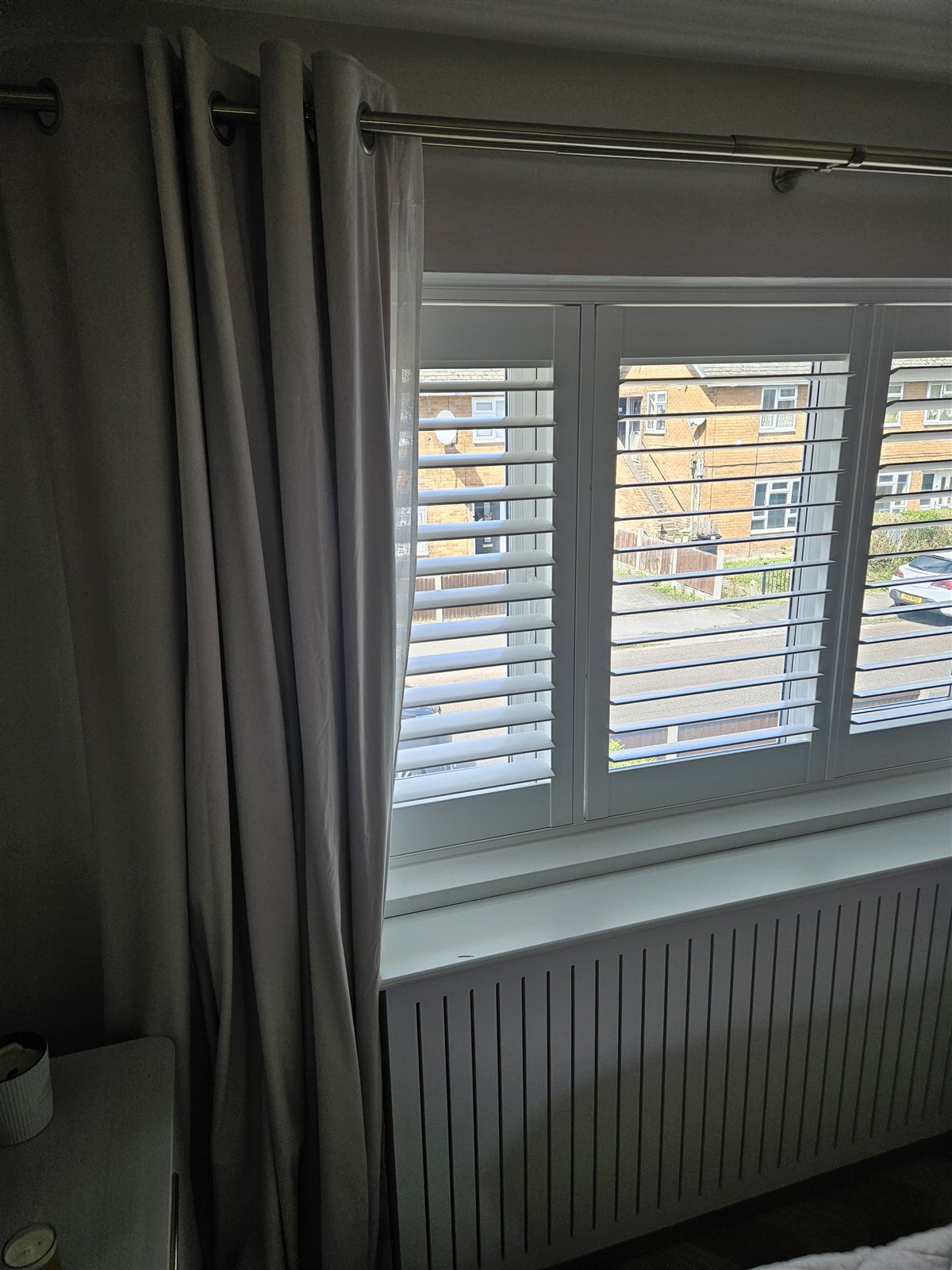 Close-up of Hampton shutter louvres beside grey bedroom curtains, fitted by Eclipse SBC in Retford