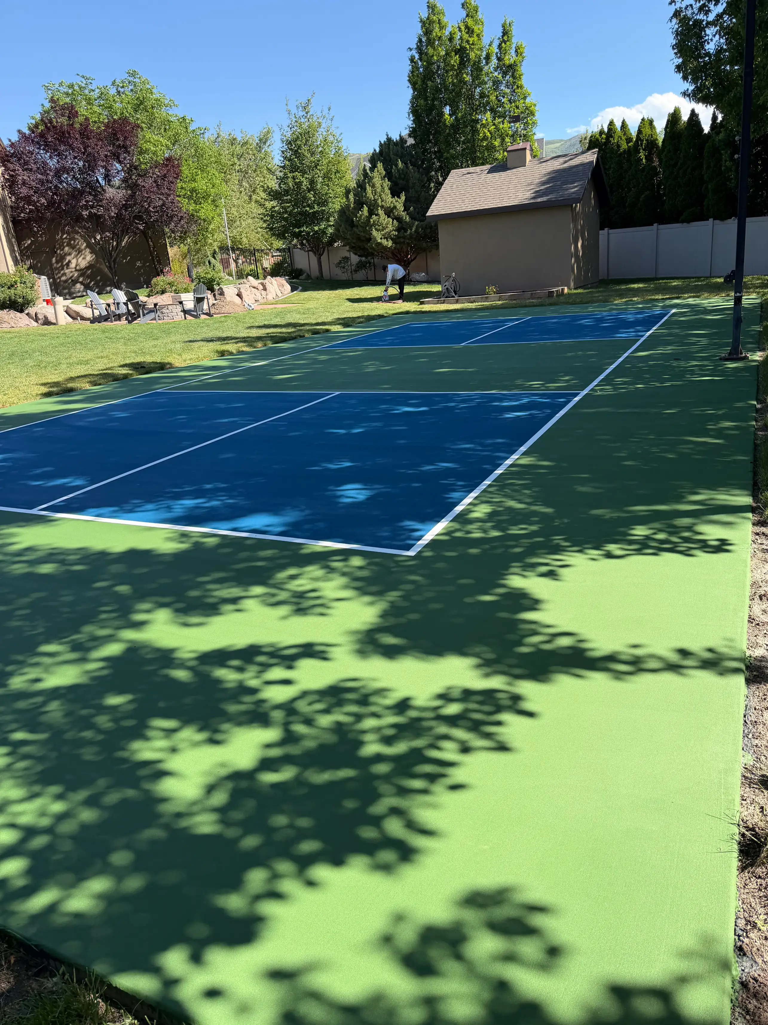 Navy and green pickleball court in a tree-shaded backyard