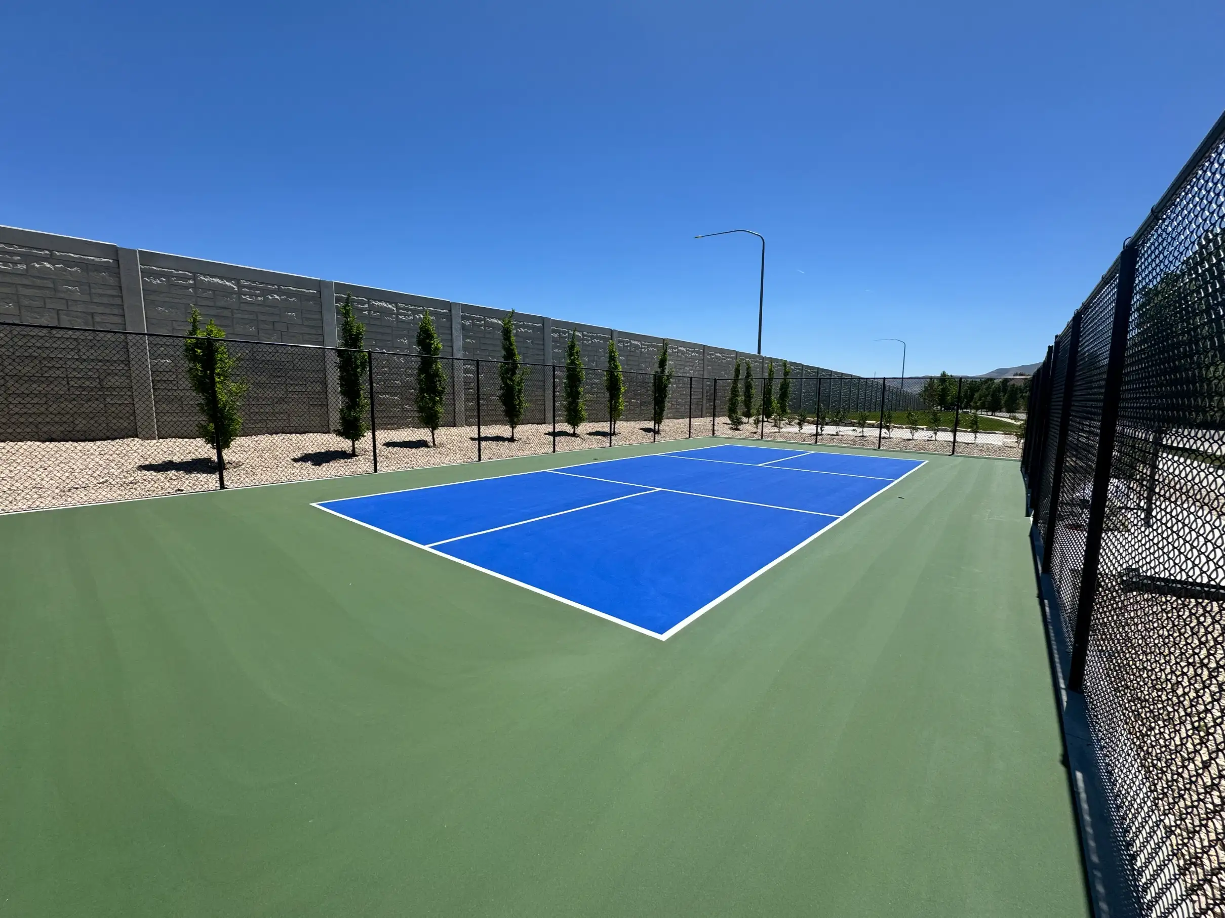 Royal blue and green fenced pickleball court beside a stone sound wall