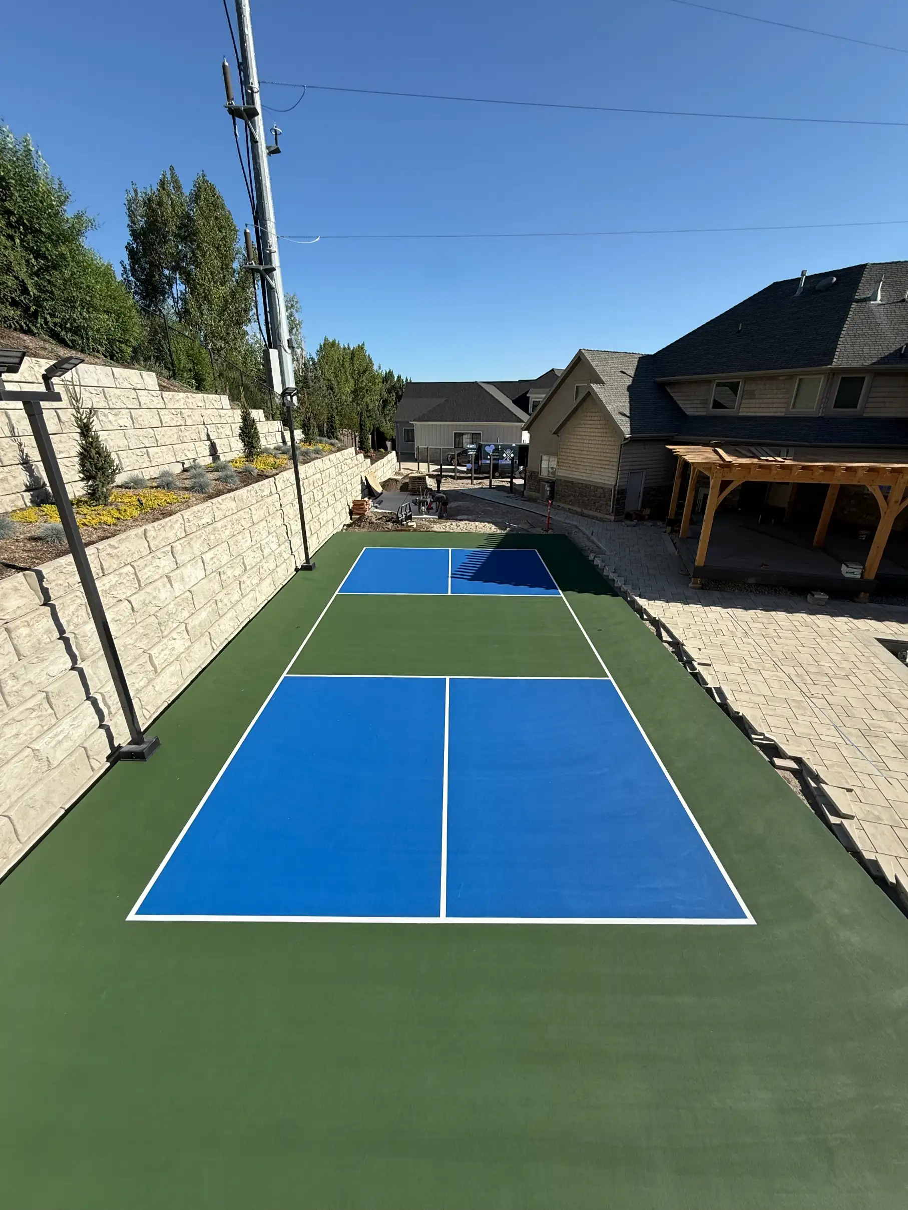 Blue and green pickleball court with court lights along tiered stone walls