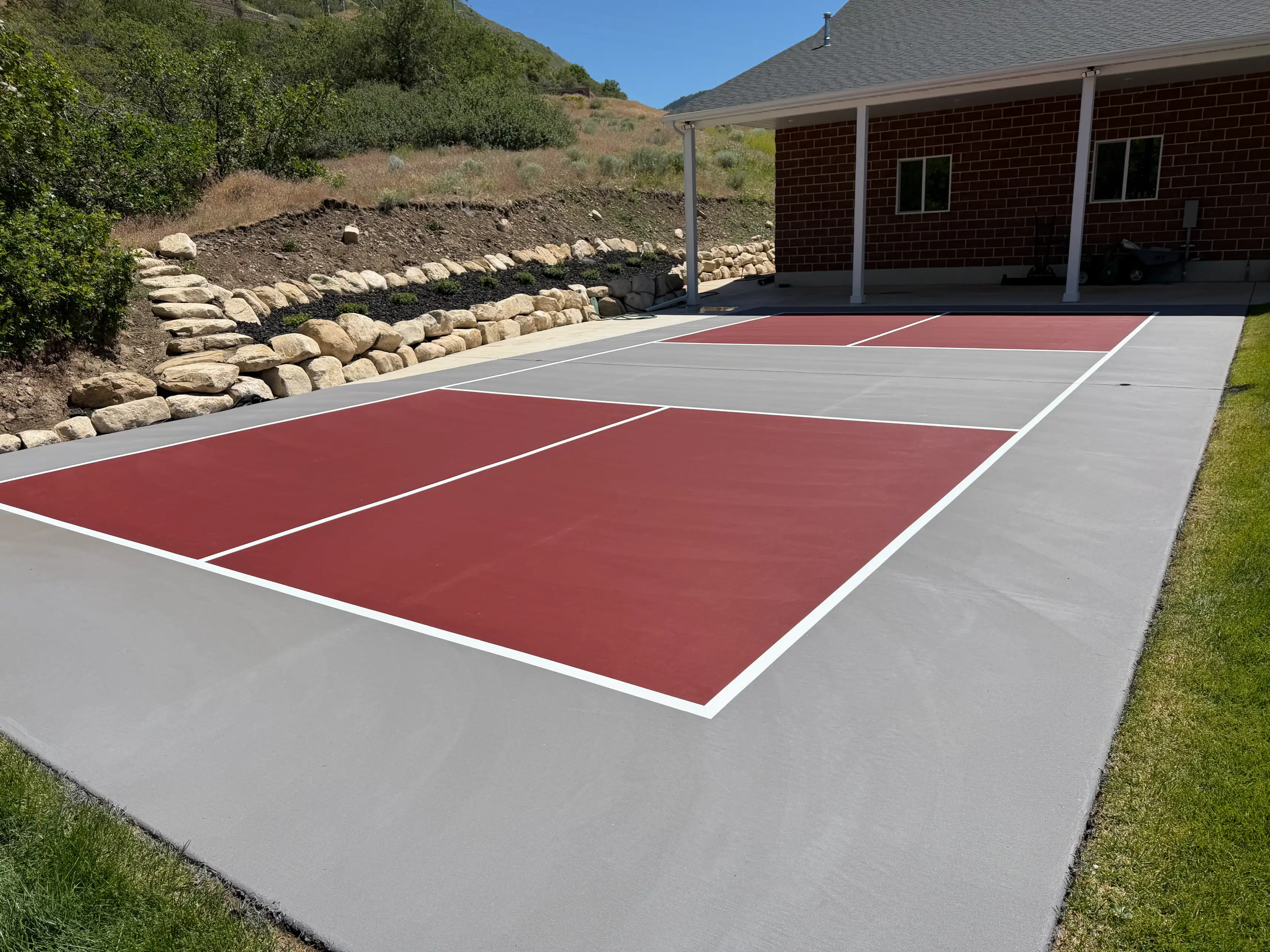 Crimson and grey pickleball court beside a boulder retaining wall