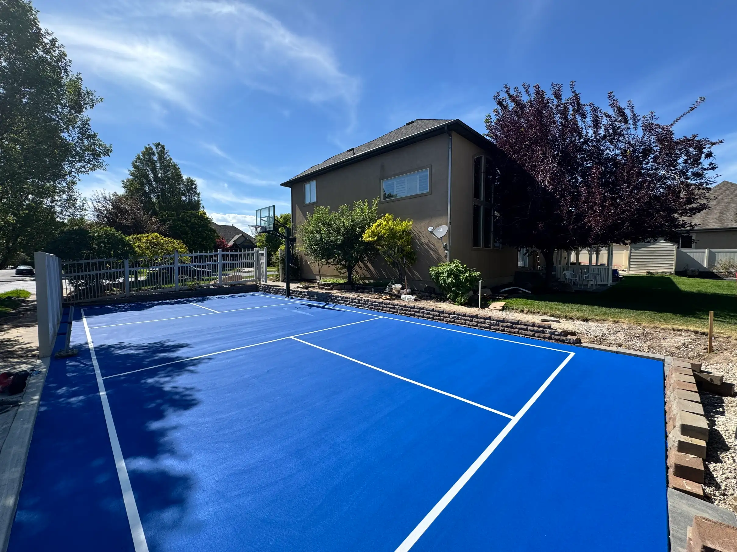 Bright blue side-yard pickleball court with basketball hoop
