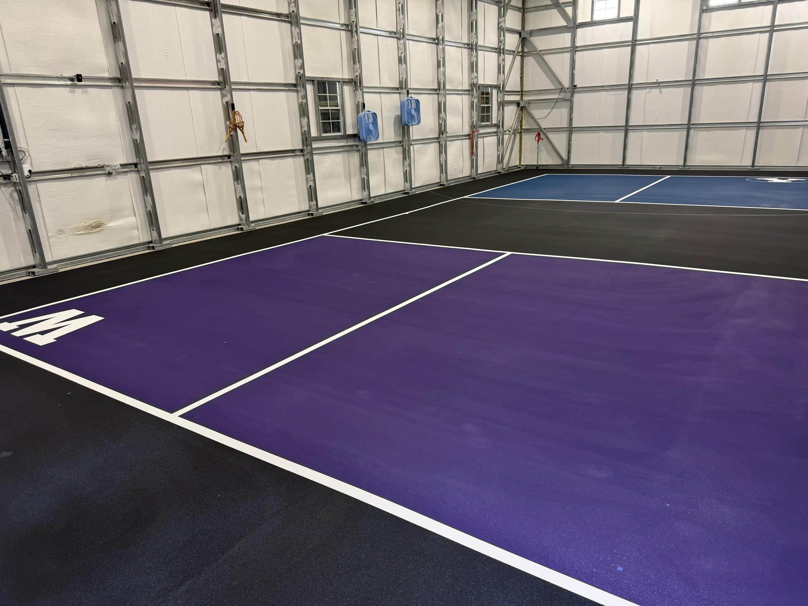 Indoor purple and black pickleball courts inside a steel-frame facility