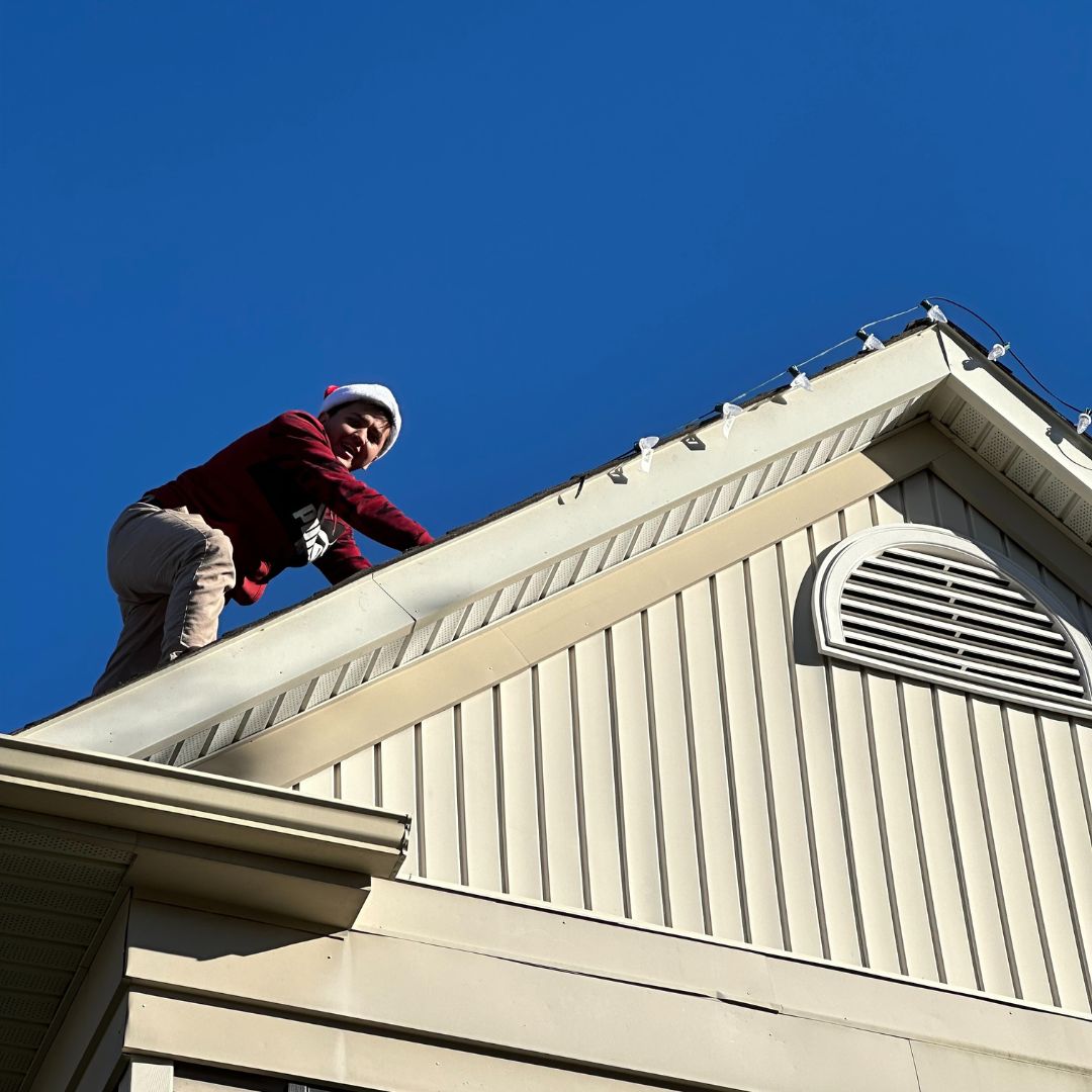 Professional Christmas light installer safely working on residential roofline - Golden Glow Christmas Lights NJ