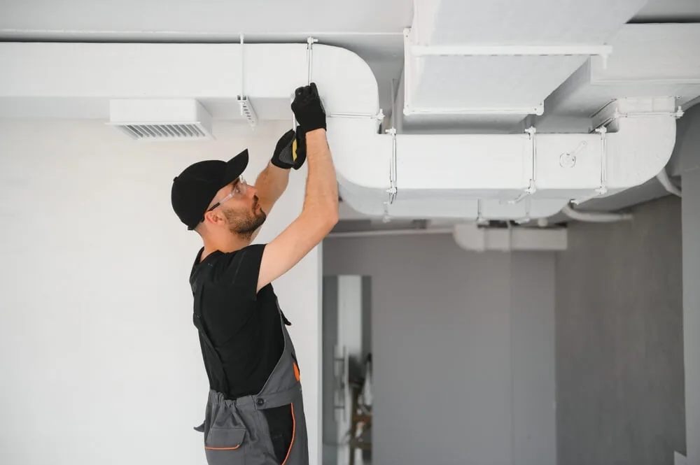 Técnico HVAC inspeccionando y ajustando conductos de aire